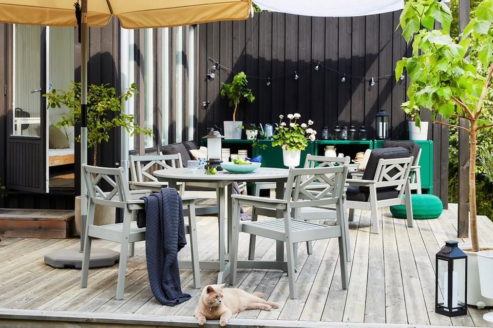Erhöhte Terrasse mit Holzboden und den Gartenmöbeln "Bondholmen" von Ikea vor einer schwarzen Fassade