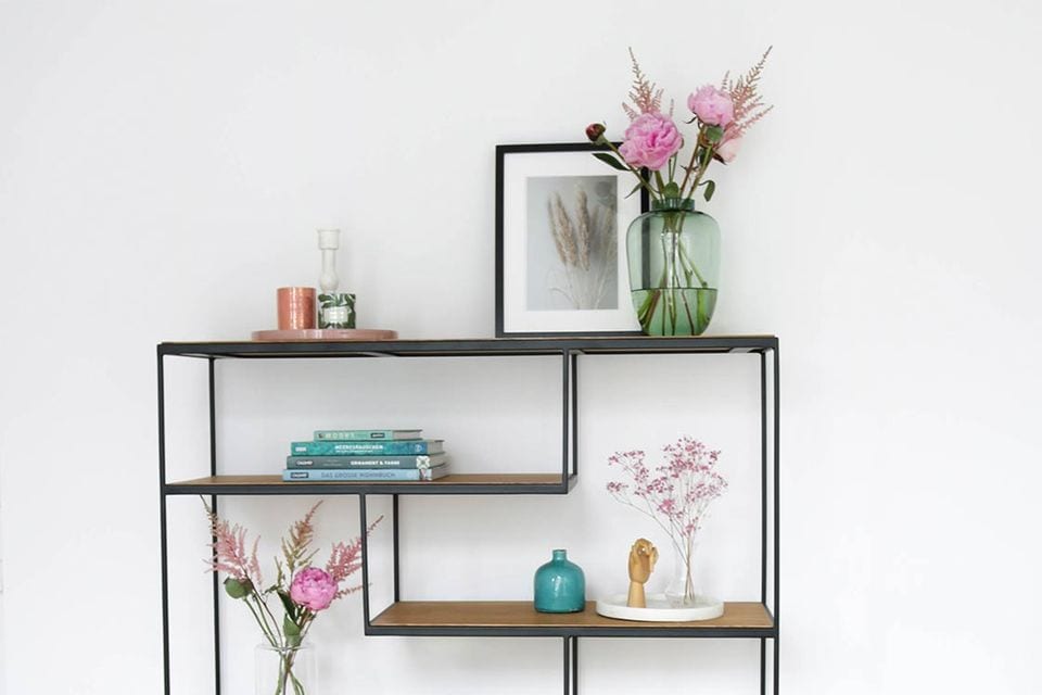 Mit Blumen und natürlichen Wohnaccessoires frühlingshaft dekoriertes, offenes Regal an einer weißen Wand