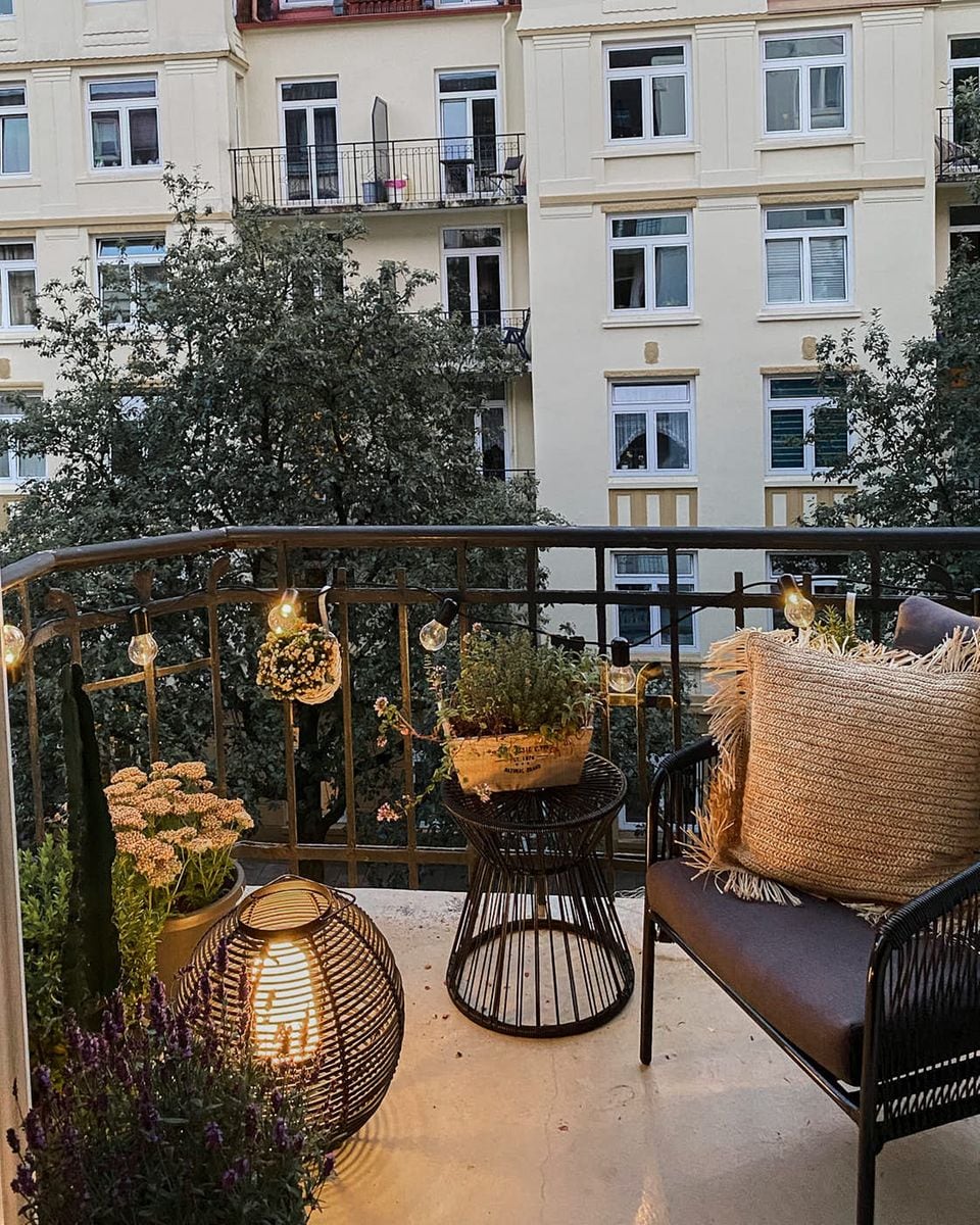 Ein Balkon ist mit Lichterkette, Bodenleuchte und verschiedenen Möbeln, Pflanzen und Textilien dekoriert