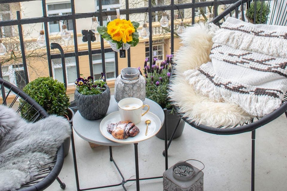 Frisch bepflanzter Balkon im Frühling mit zwei Stühlen, einem kleinen Tisch und einer Laterne