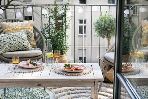 Kleiner Balkon mit Sesseln, Holztisch, Teppichen, Kissen und Balkonpflanzen