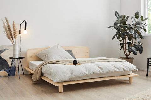 Ein Schlafzimmer mit Bett und Lampe auf der Fensterbank, daneben eine Monstera-Pflanze