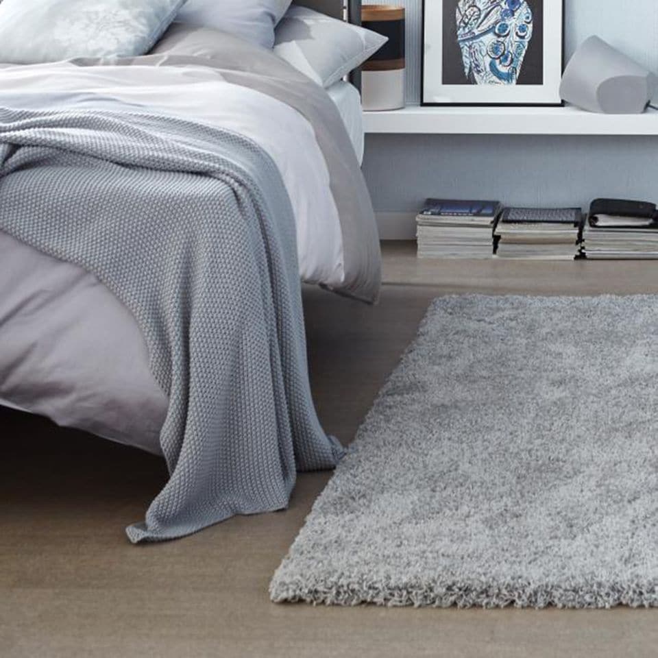 Mit Textilien dekoriertes Bett und einem tiefen Regalbrett rechts davon mit zusätzlichem Stauraum