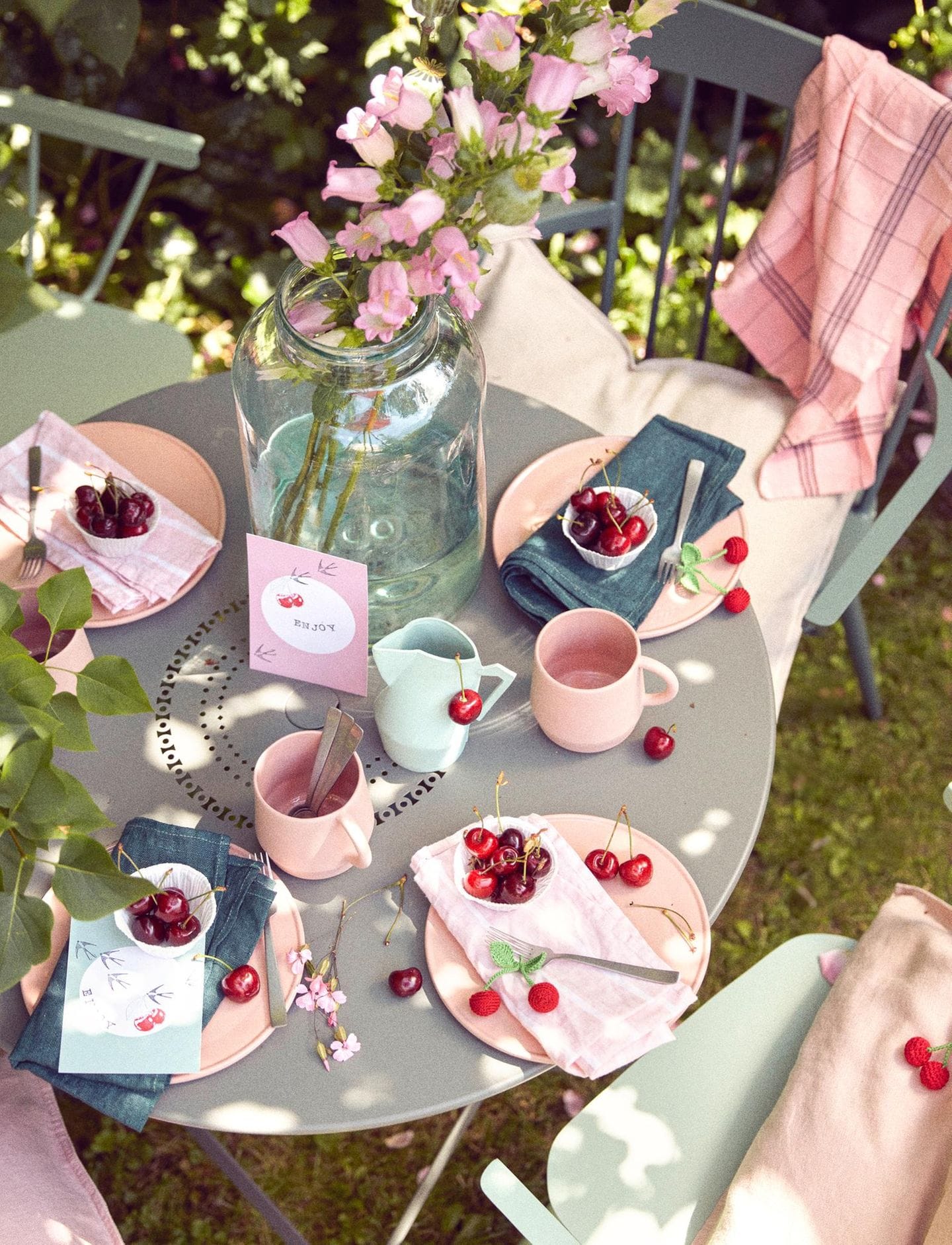 Gedeckter Gartentisch mit Geschirr und Tischkarten sowie Deko mit Kirschmotiven