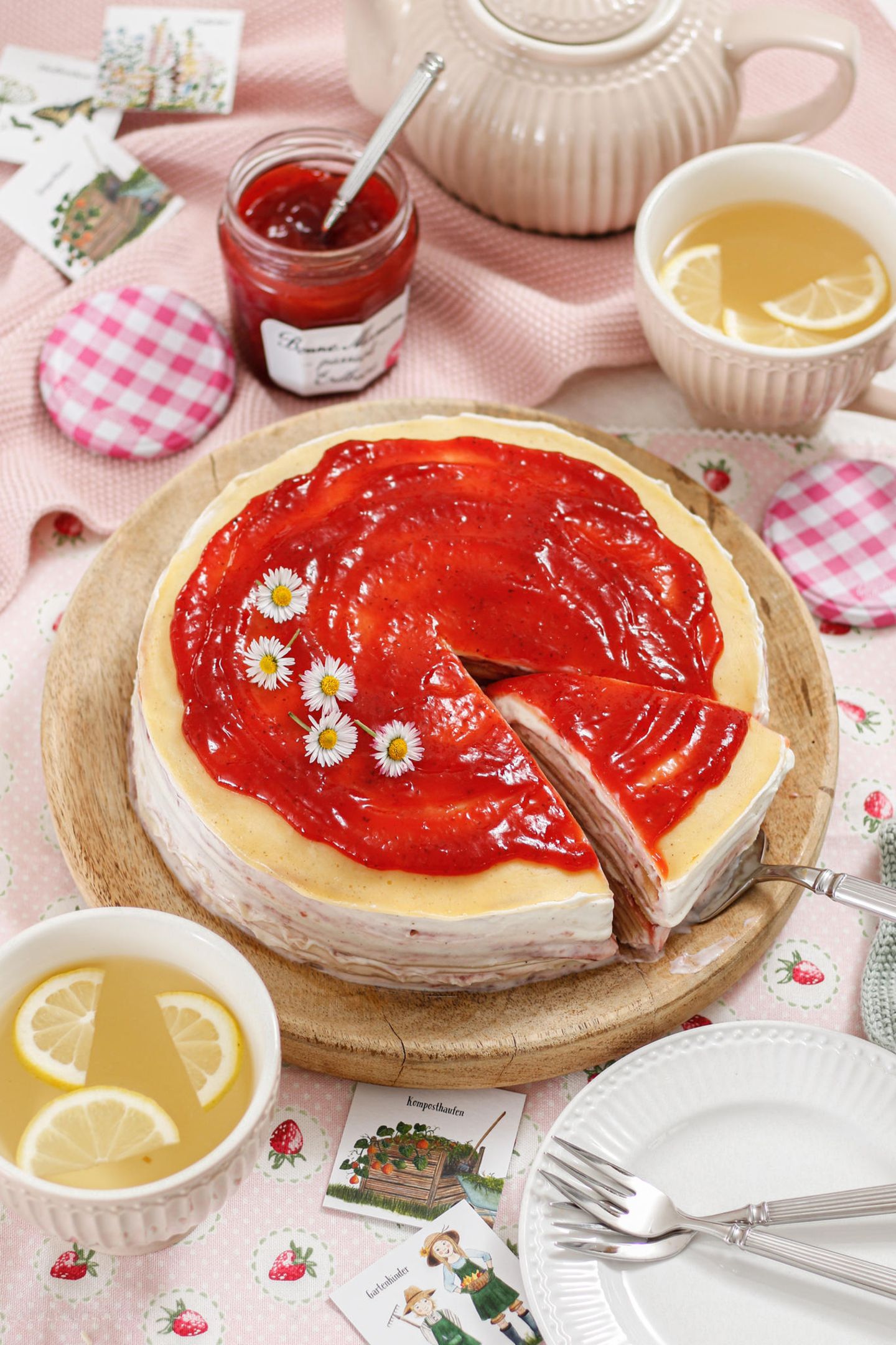 Eine Torte aus Crêpes mit Erdbeer-Creme und einer Schicht Marmelade steht auf einem gedeckten Kaffeetisch