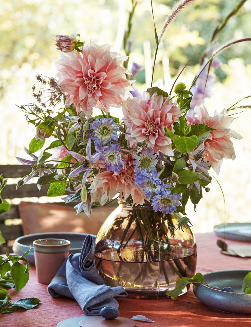 Blumenstrauß mit Dahlien in einer getönten Glasvase auf einem gedeckten Tisch