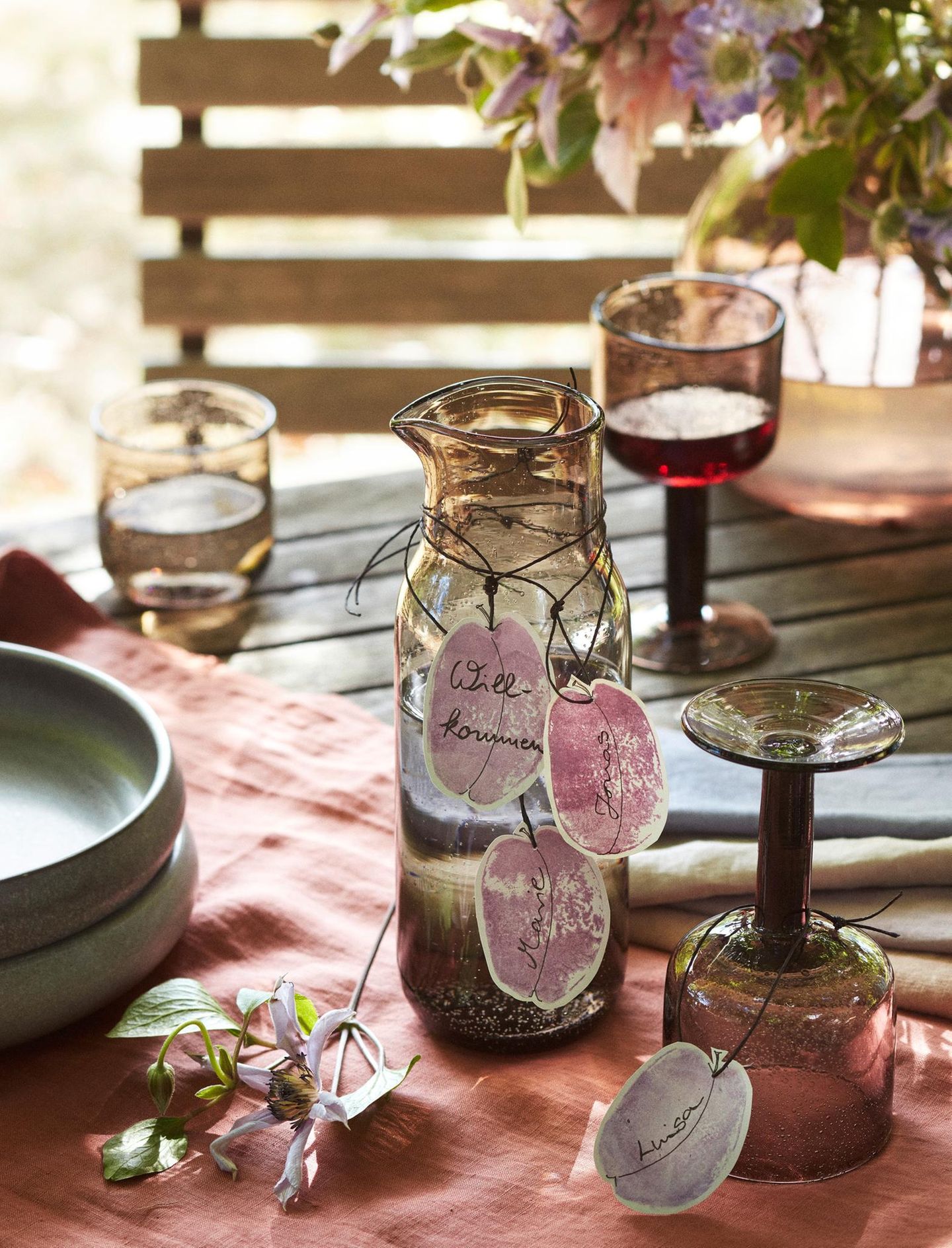 Wasserkanne und Gläser auf einem Tisch mit Tischdecke und Geschenkanhängern in Pflaumenform