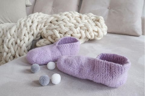 Selbst gestrickete lila Filzschuhe auf einem grauen Sofa