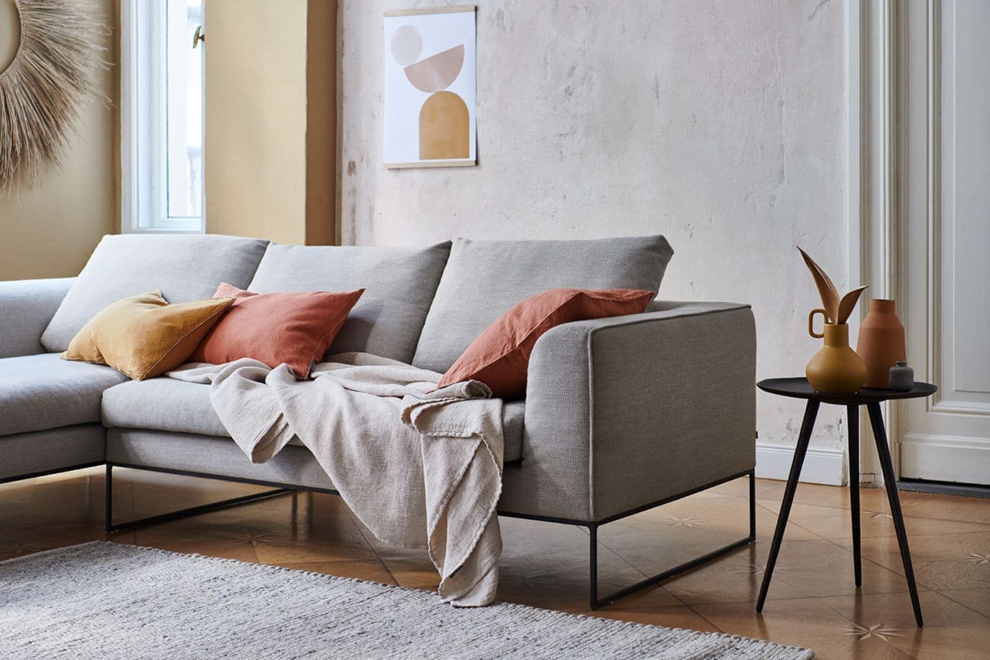 Graues Sofa mit Kissen in Erdtönen, einem Plaid und einem grauen Teppich