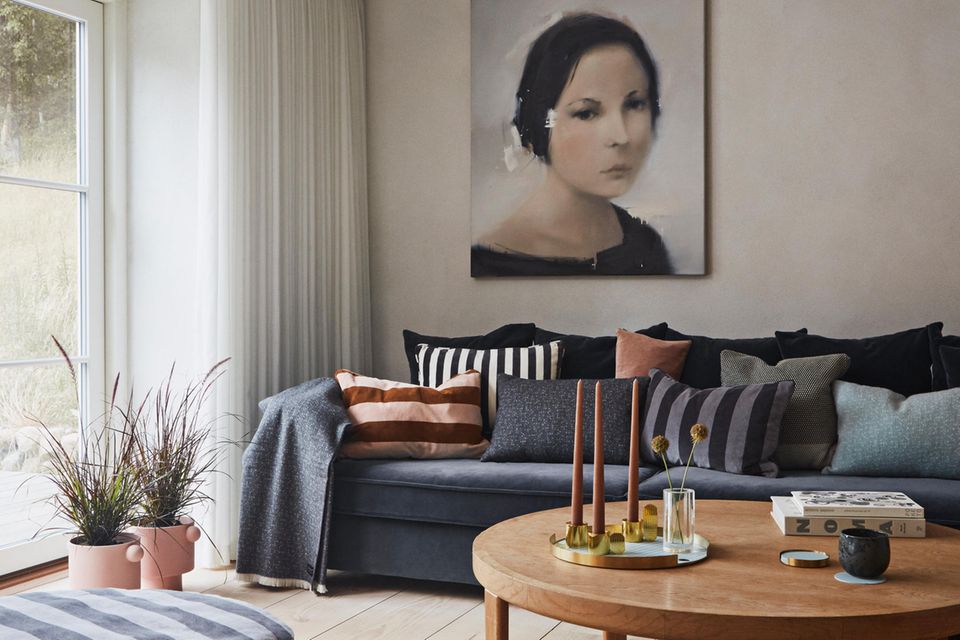 Gemütliches Wohnzimmer mit blauem Sofa eingerahmt von Wohnaccessoires wie Kissen, Decken, Kerzenhaltern und Pflanztöpfen