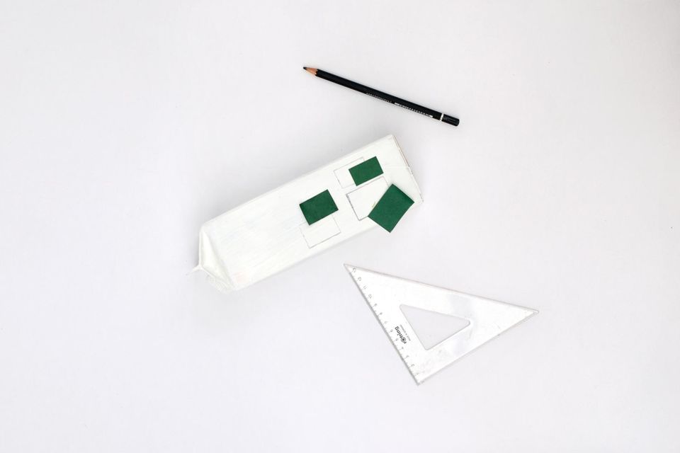 Weißer Tetra-Pak-Karton mit grünen Schablonen aus Pappe, daneben ein Stift