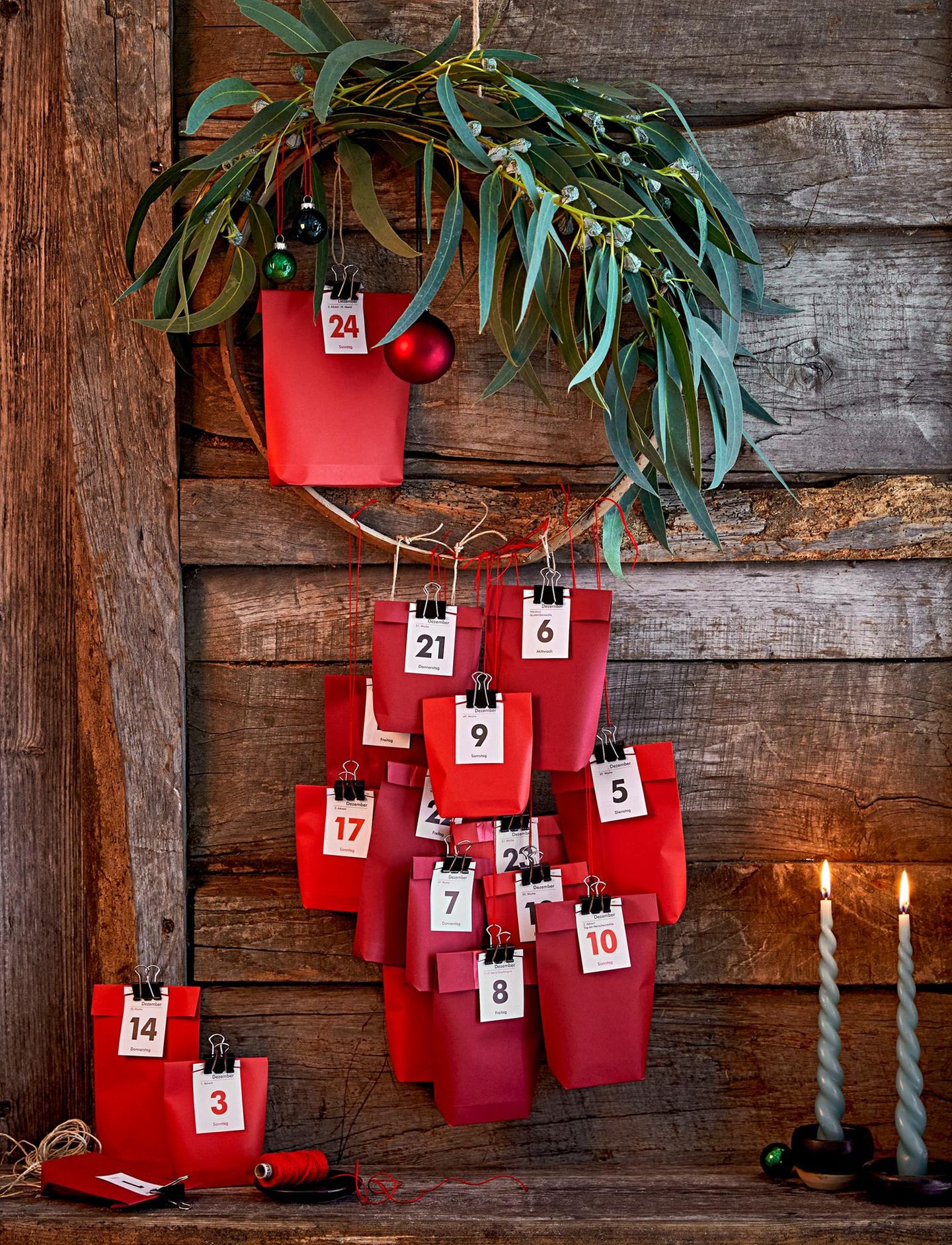 Rote Tütchen mit weißen Zahlenkärtchen als Adventskalender hängen an einem Weidenkranz mit Eukalyptus