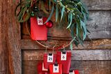 Rote Tütchen mit weißen Zahlenkärtchen als Adventskalender hängen an einem Weidenkranz mit Eukalyptus