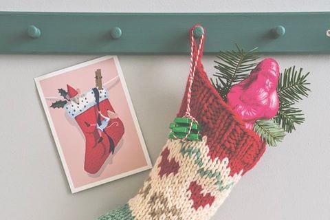 Gestrickte Socke mit weihnachtlichem Muster hängt an einer Garderobenleiste, daneben eine Postkarte