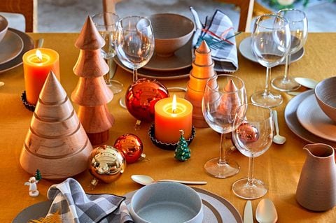 Weihnachtlich gedeckter Tisch mit Geschirr, Weingläsern, gelben Kerzen, Holztannenbäumen und Christbaumkugeln