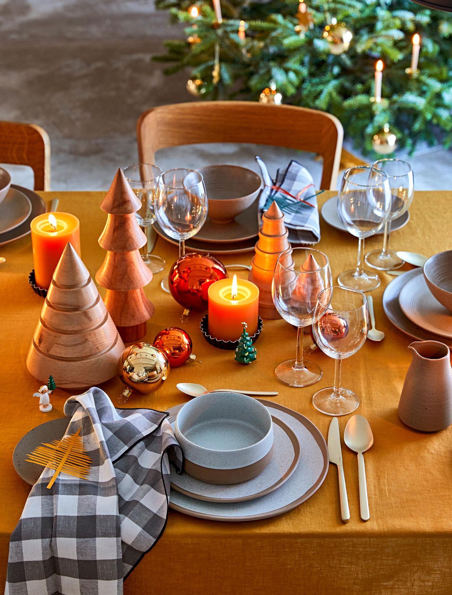 Weihnachtlich gedeckter Tisch mit Geschirr, Weingläsern, gelben Kerzen, Holztannenbäumen und Christbaumkugeln