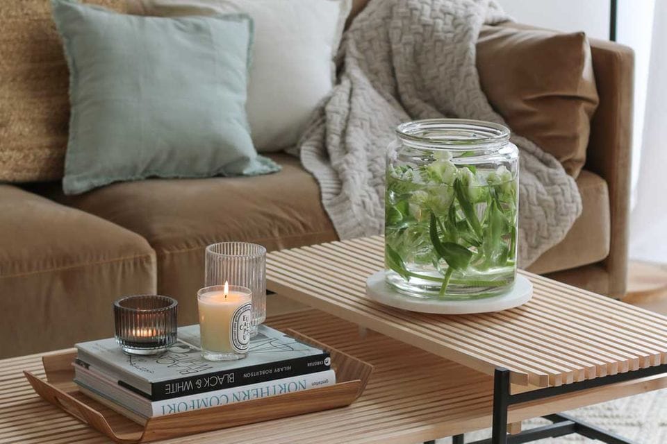Wohnzimmer mit brauner Couch und Holztisch mit Kerzen und Büchern und einem großen Glas mit Wasser und Tulpen