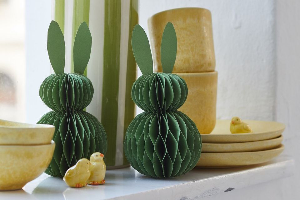 Grüne Hasenfiguren aus Papier vor einer gestreiften Vase