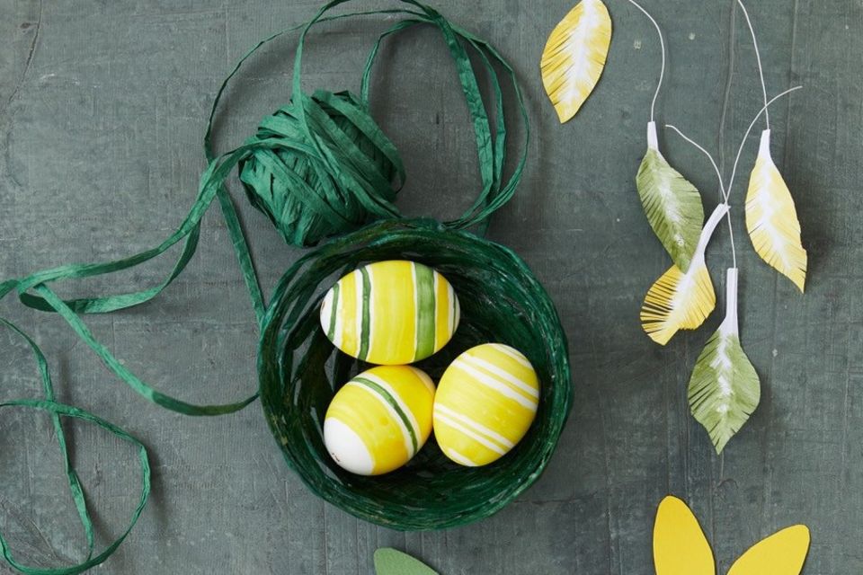 Grünes Nest aus Papierbast mit drei gelben Eiern