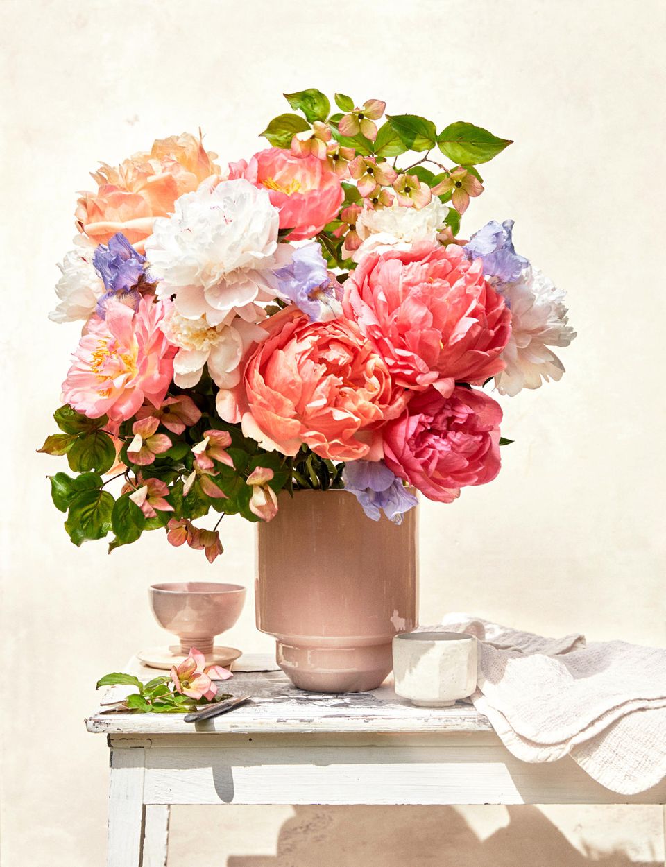 Blumenstrauß mit Pfingstrosen, Iris und Blumenhartriegel steht in einer rosa Vase auf einem Holzmöbel