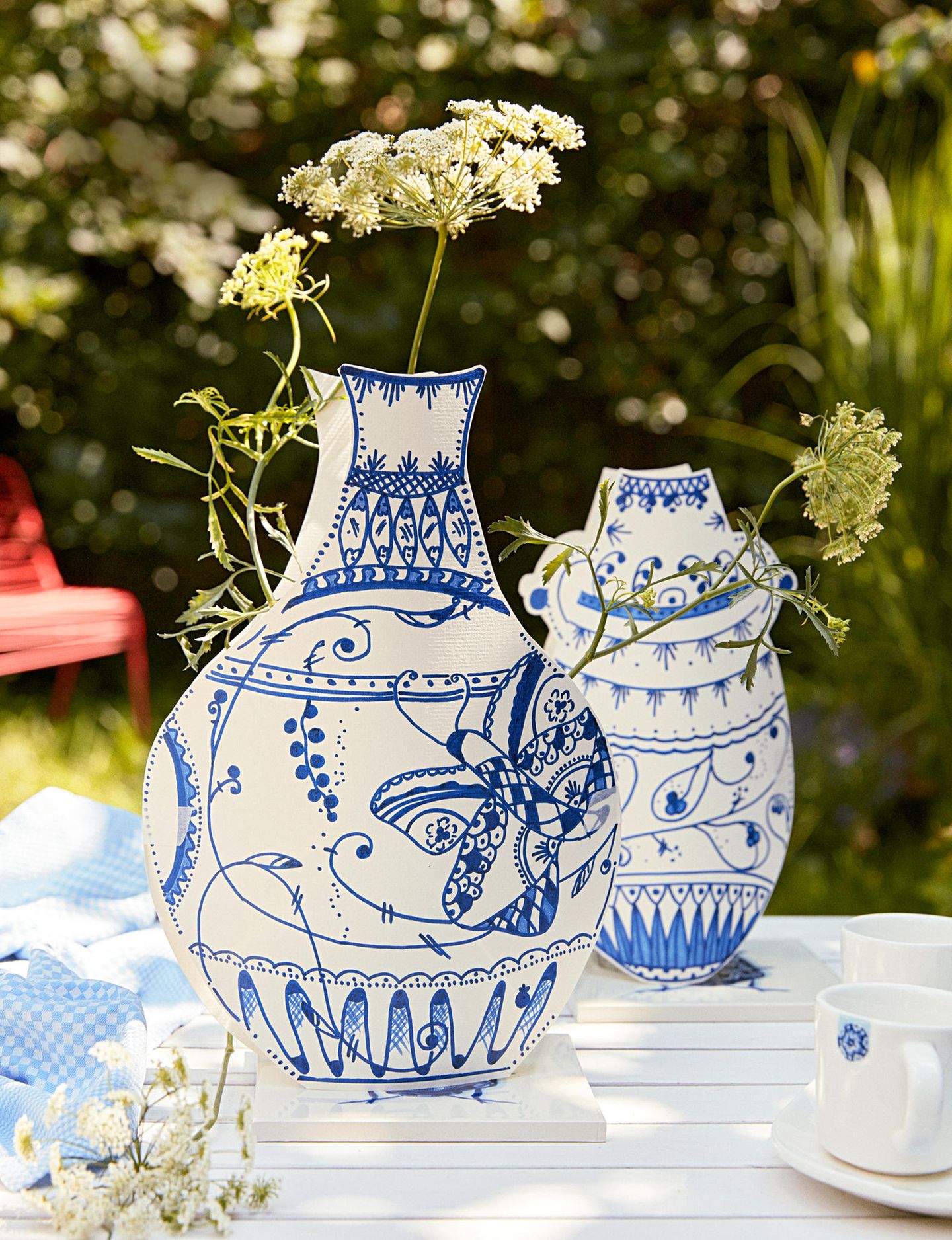 Vasen aus Papier mit blauer Verzierung auf einem Tisch mit Blumen
