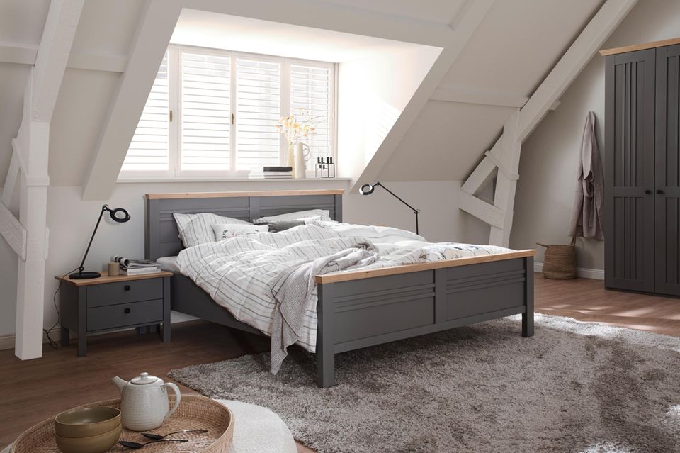 Graues Bett unter einer Dachschräge mit Fenster