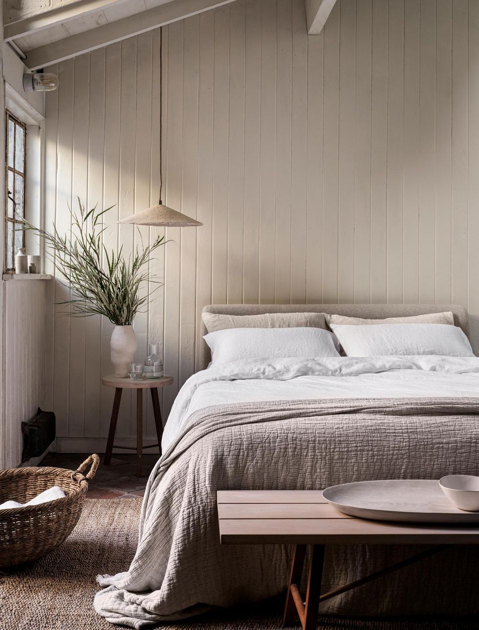 Bett mit Leinenbettwäsche, dahinter Wand aus Holz, Pflanze und Beistelltisch
