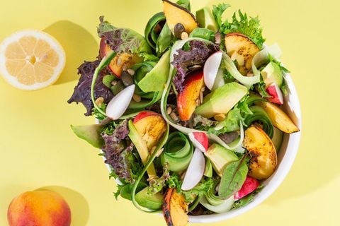 Salat mit Mango und Pfirsich und Avocado in einer Schüssel, dahinter gelber Hintergrund und Früchte verteilt
